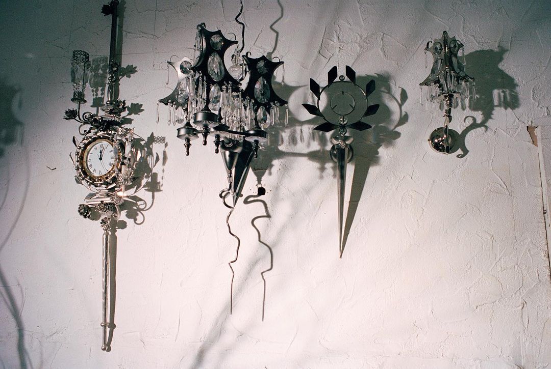 Four ornate sconces are mounted on a textured white wall. These fixtures feature clock faces, crystals, and decorative metalwork.