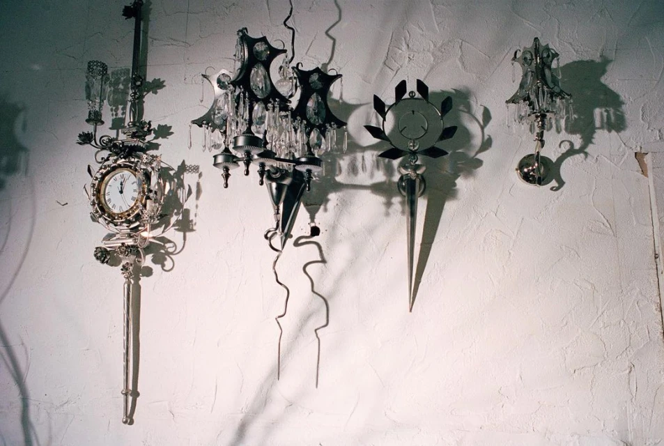 Four ornate sconces are mounted on a textured white wall. These fixtures feature clock faces, crystals, and decorative metalwork.