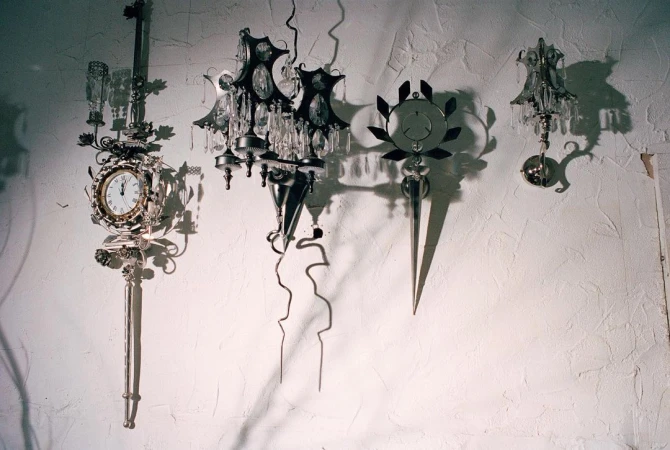 Four ornate sconces are mounted on a textured white wall. These fixtures feature clock faces, crystals, and decorative metalwork.