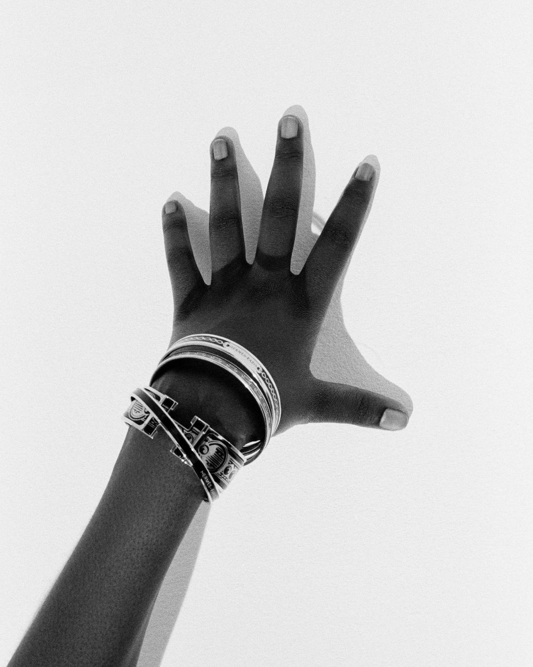 Close-up monochrome image of a hand wearing stacked silver metal bangles against a plain white background by Camille Vivier