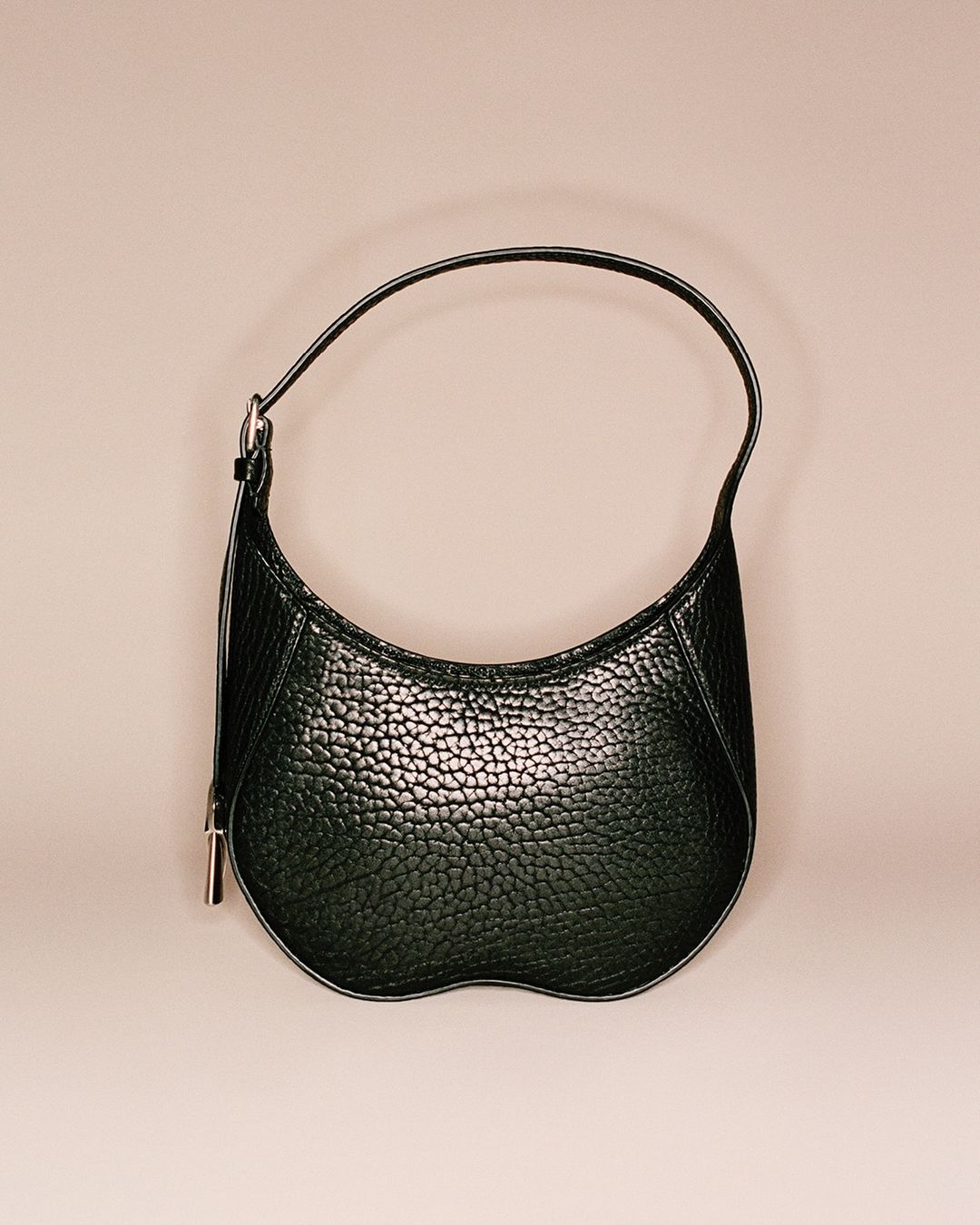 Stylish black pebbled leather handbag with a curved shape and a single handle, displayed against a soft, neutral background. Fashion accessory.
