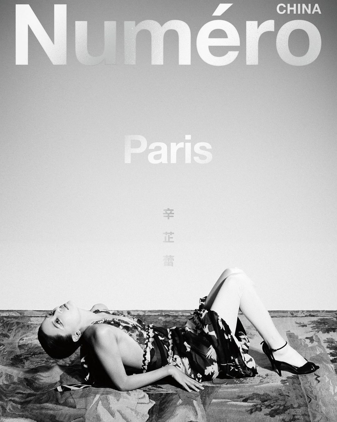 Fashion editorial featuring a supine woman in a dress and heels, lying on a patterned surface, against a gray gradient background with magazine text.