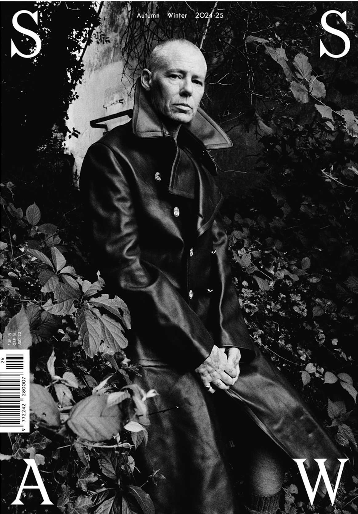 Black and white magazine cover featuring a mature adult male in a dark coat standing in a leafy outdoor environment, evoking a somber mood.