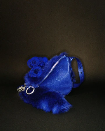 Fashion still life of a blue leather purse trimmed with blue fur and decorated with blue roses against a dark background.