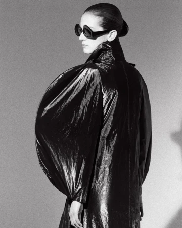 Black and white portrait of a woman wearing sunglasses and a shiny, puffy coat. Fashion shot in a photo studio with cool tone.