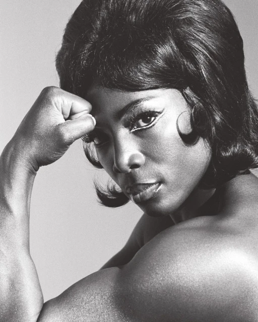 Monochrome portrait of an African American woman with short, dark hair, flexing her arm to display strong biceps and shoulder muscles.