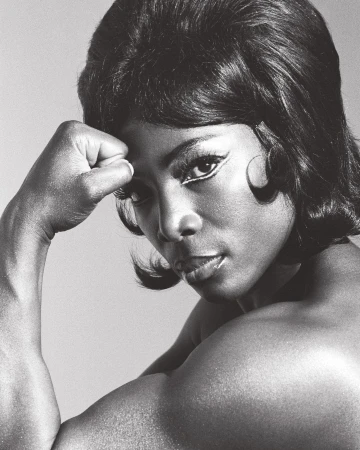 Monochrome portrait of an African American woman with short, dark hair, flexing her arm to display strong biceps and shoulder muscles.