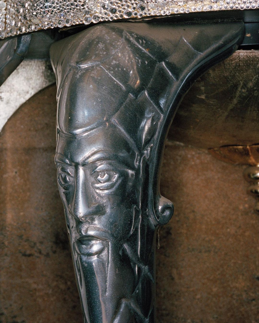 Close-up of a dark metal furniture leg with a stylized, ornate face design, part of an antique or decorative piece.