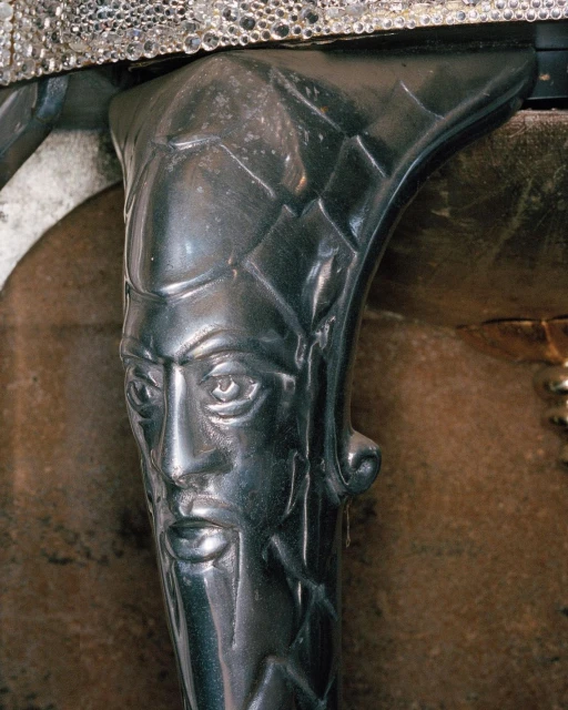 Close-up of a dark metal furniture leg with a stylized, ornate face design, part of an antique or decorative piece.