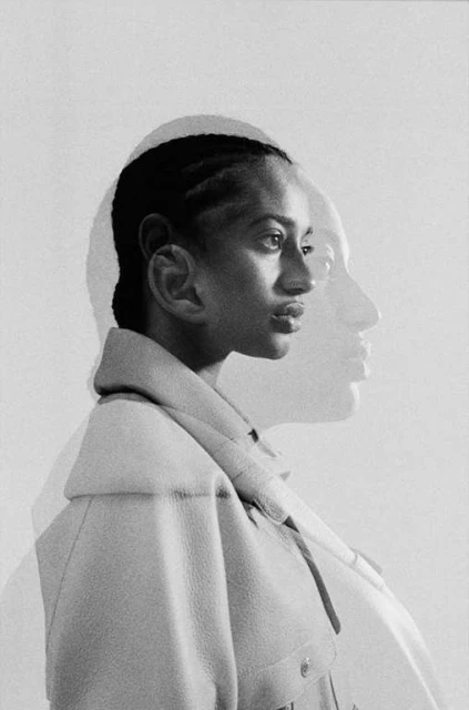 Monochromatic portrait of a woman with braided hair wearing a collared jacket, profile view, with a soft-focus double exposure effect.