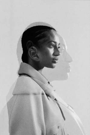 Monochromatic portrait of a woman with braided hair wearing a collared jacket, profile view, with a soft-focus double exposure effect.