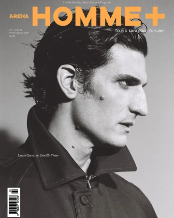 Arena Homme+ magazine cover featuring a close-up of Louis Garrel in a dark coat against a neutral gray background.