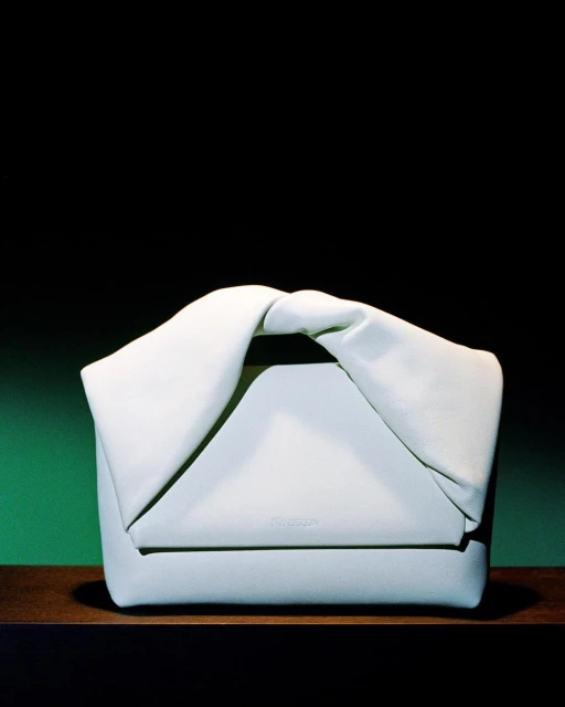 Close-up studio shot of a stylish light green leather handbag featuring a unique twisted handle design, set against a dark background.