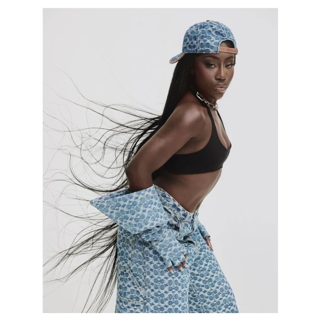 Studio shot of an African-American woman in a patterned baseball cap and jacket, with long flowing hair against a white backdrop.