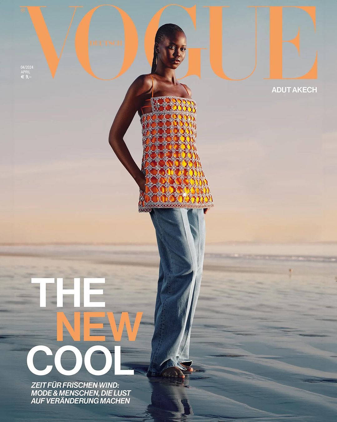Vogue cover featuring an African woman in a beaded top and wide-leg jeans, standing on a reflective beach with a pastel sky backdrop.