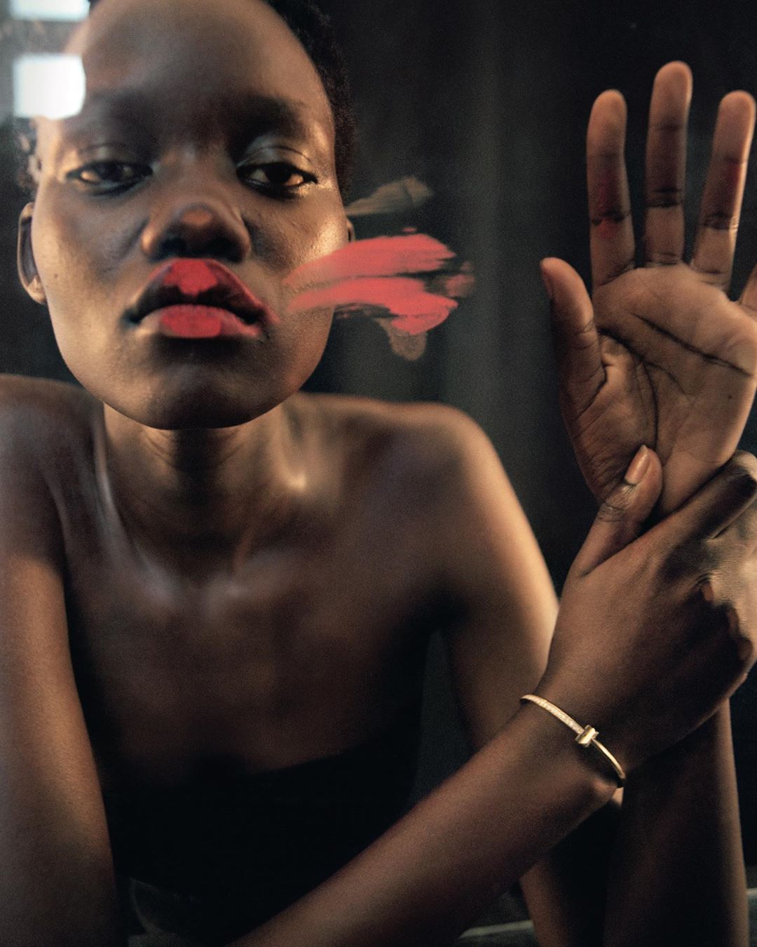 Portrait of an African woman with red lipstick and a gold bracelet, her hand is on a window with smeared lipstick.