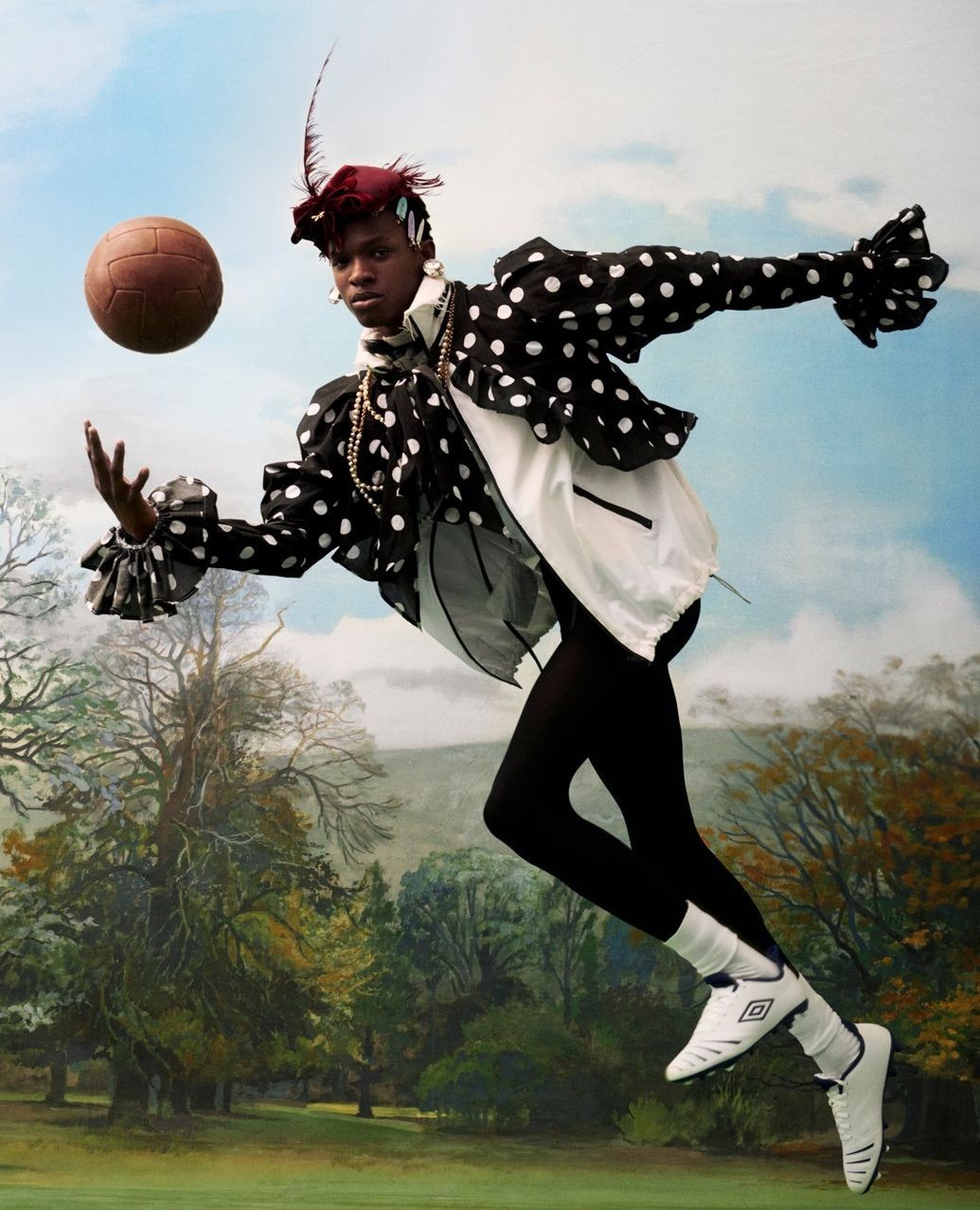 An adult female in elaborate polka dot costume kicks an antique soccer ball in a surreal outdoor setting.