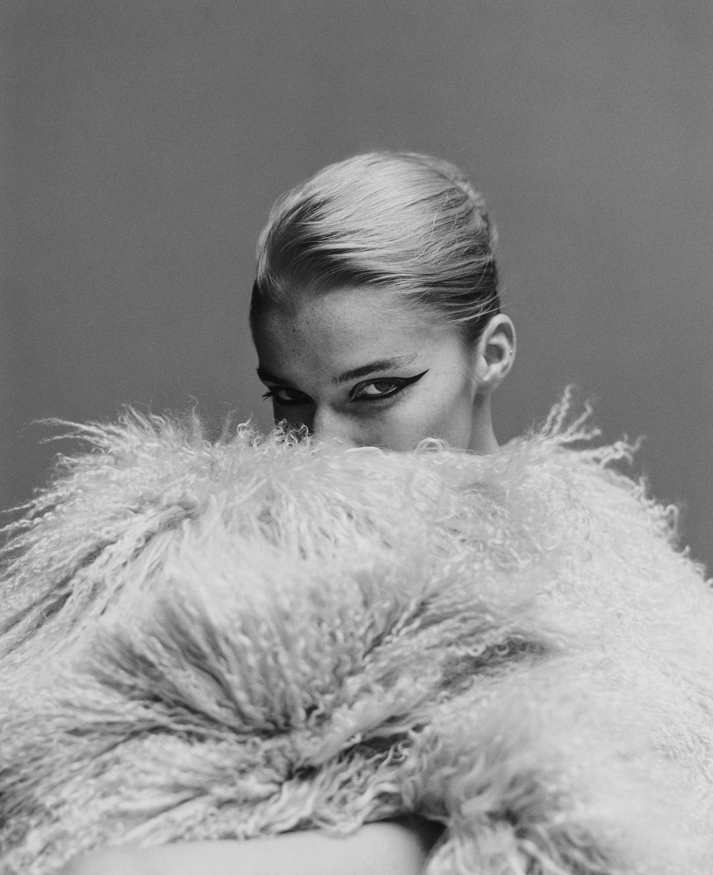 Portrait of a blonde woman holding a large fluffy textured coat up to obscure her face by photographer Campbell Addy.