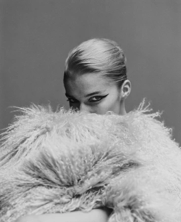 Portrait of a blonde woman holding a large fluffy textured coat up to obscure her face by photographer Campbell Addy.