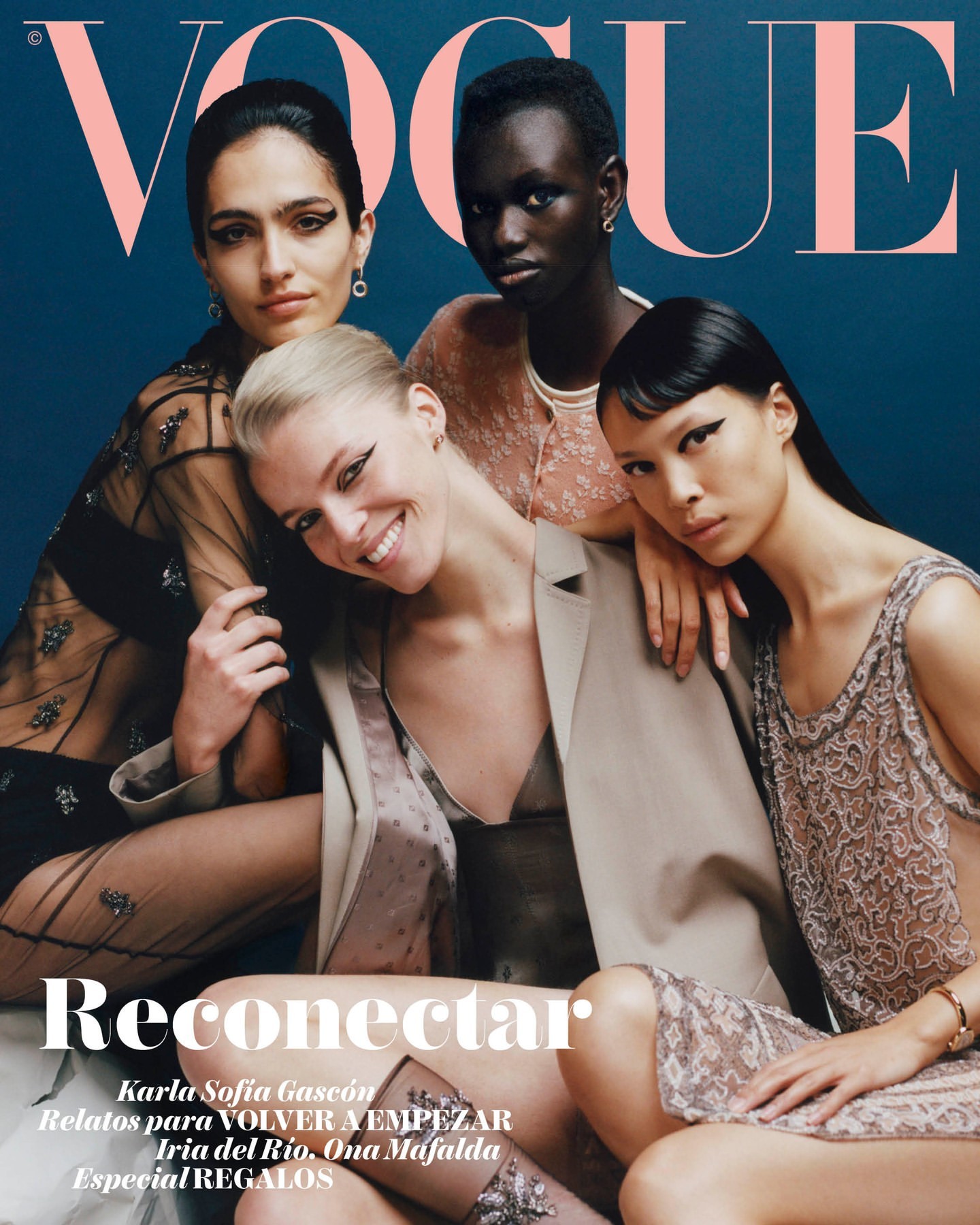 Group of four female fashion models posing together for a magazine cover portrait against a dark blue background in London.