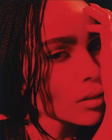 Close-up portrait of Zoe Kravitz bathed in dramatic red light with braided hair and hand raised to her forehead