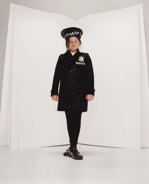 Young girl in a police uniform standing against a white backdrop, posing for a full-length portrait in a studio setting.