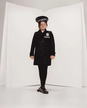 Young girl in a police uniform standing against a white backdrop, posing for a full-length portrait in a studio setting.
