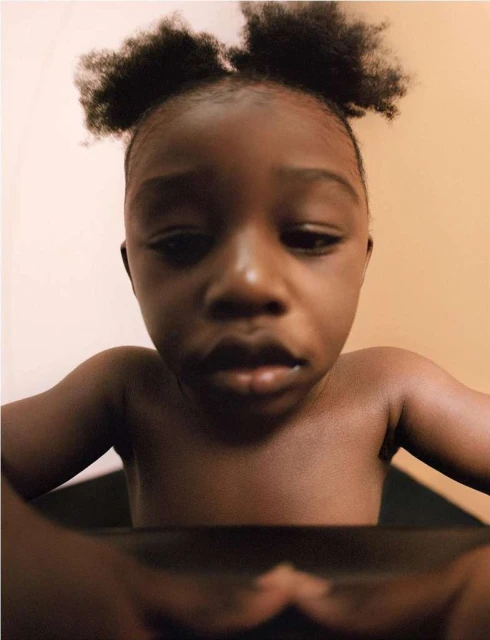 Portrait of a dark-skinned child with afro puffs, focusing on facial details and skin tone, indoors with soft natural lighting.