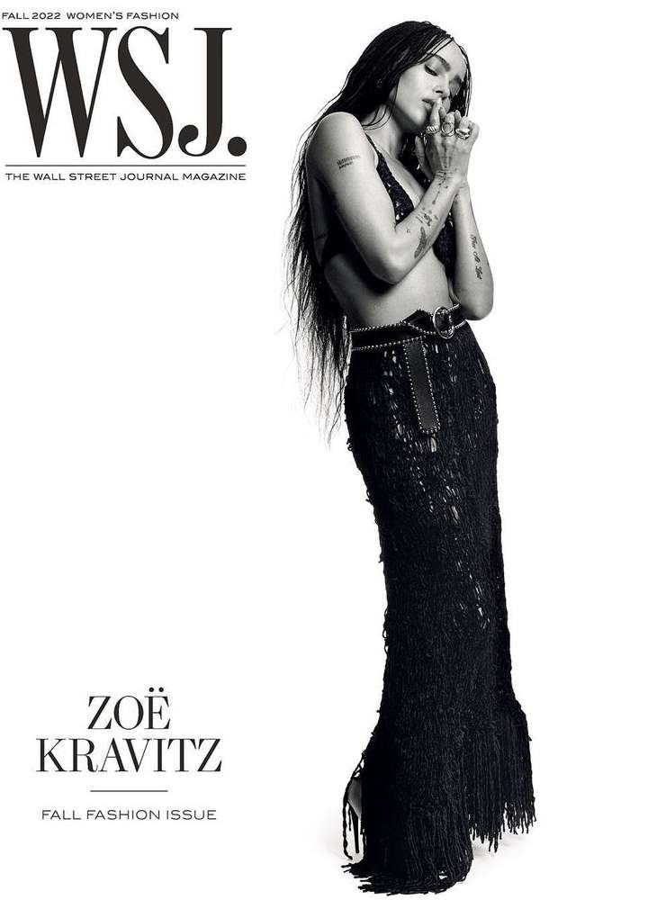 Zoë Kravitz poses in a black two-piece outfit and skirt for a black-and-white magazine cover, standing against a clean, bright background.