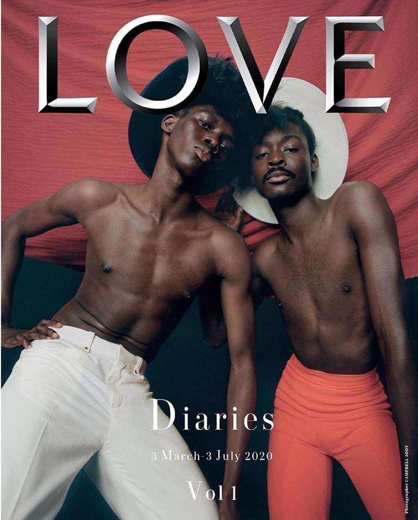 Two dark-skinned shirtless men in a magazine cover, one in white pants and the other in coral pants, with the word LOVE written on top.
