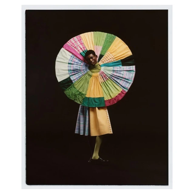 Fashionable Black model poses in a colorful, patterned dress with matching legwear against a dark backdrop in a photo studio setting.