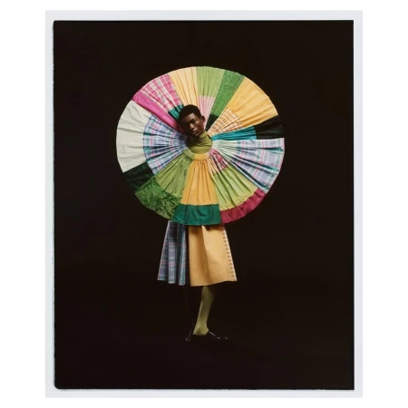 Fashionable Black model poses in a colorful, patterned dress with matching legwear against a dark backdrop in a photo studio setting.