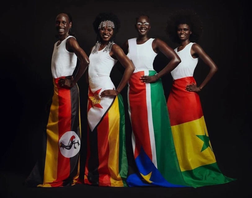 Four African women pose wearing dresses made of country flags on a dark background, smiling. Fashion and national pride concept.