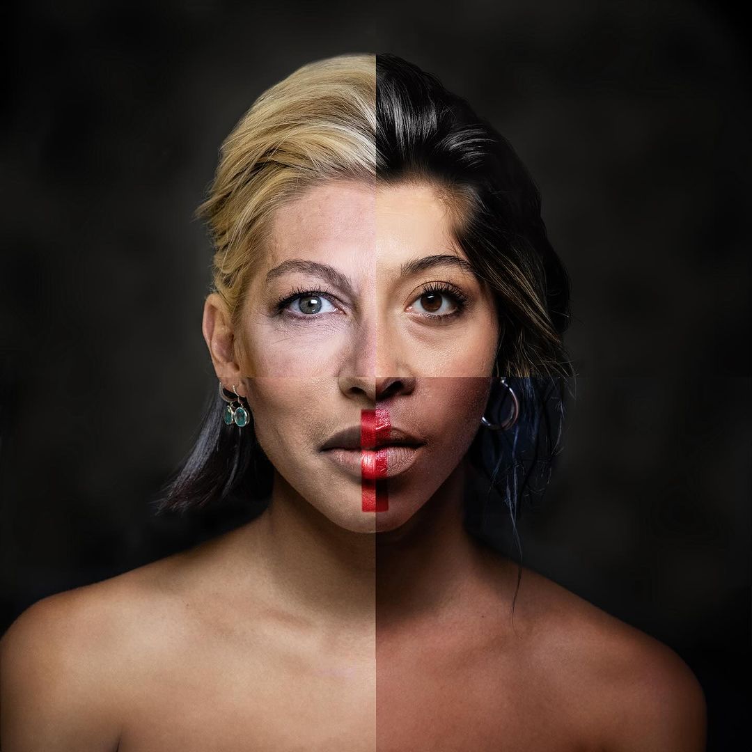 Portrait of a woman with dual-tone makeup and hair, split into black and blonde sections, featuring contrasting skin tones on a dark background.