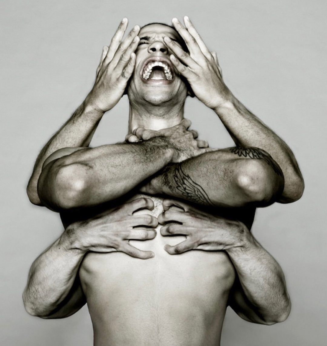 Monochrome studio portrait of a shirtless adult male with multiple arms and hands holding his head, neck and chest.