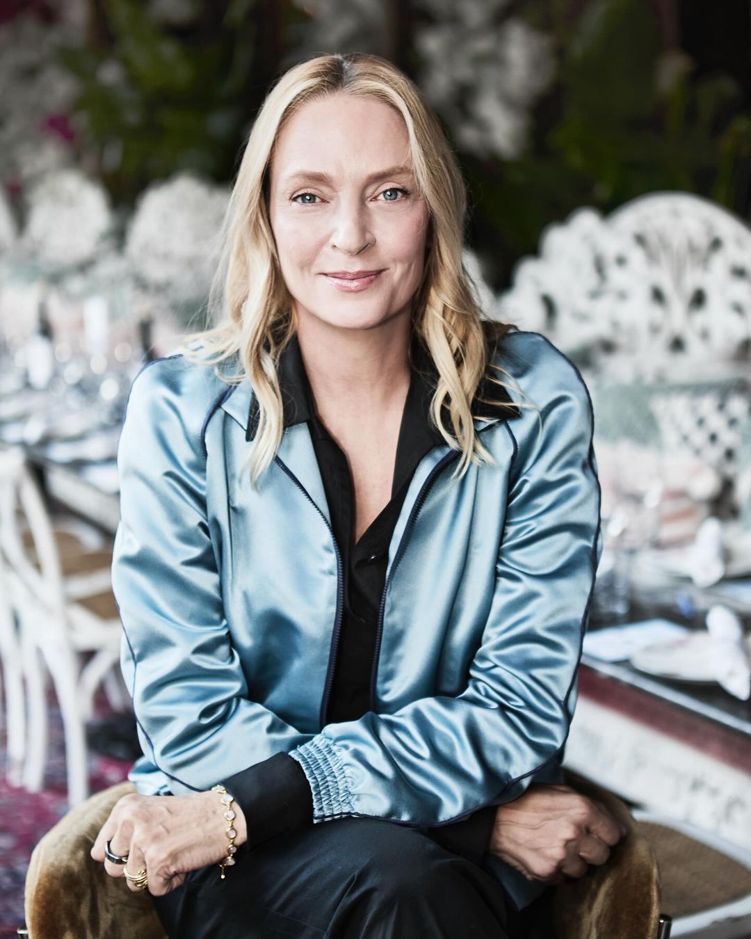 Portrait of fair-skinned adult woman with blonde hair, smiling, wearing a satin blue jacket in an indoor environment.