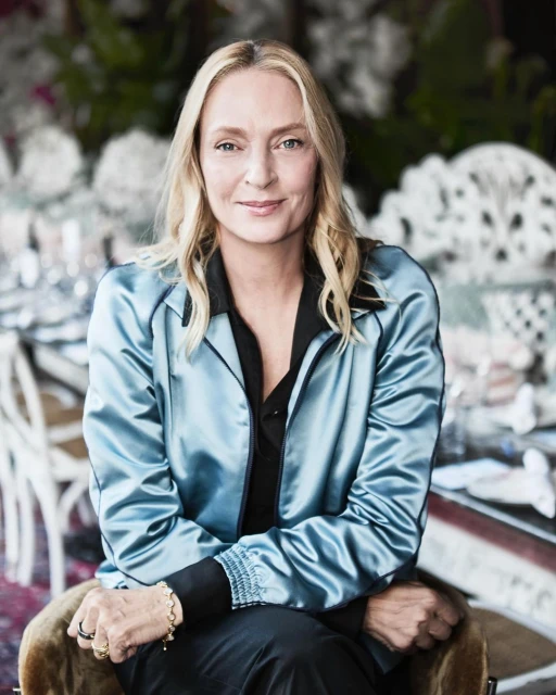 Portrait of fair-skinned adult woman with blonde hair, smiling, wearing a satin blue jacket in an indoor environment. 