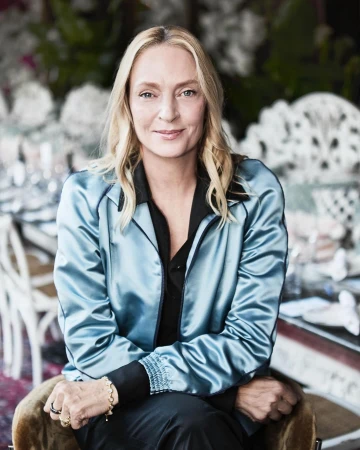 Portrait of fair-skinned adult woman with blonde hair, smiling, wearing a satin blue jacket in an indoor environment. 