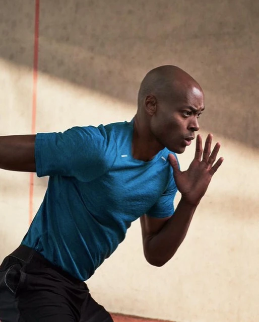 Action shot of a bald African-American male in sportswear running with determination against a neutral wall with a red stripe.