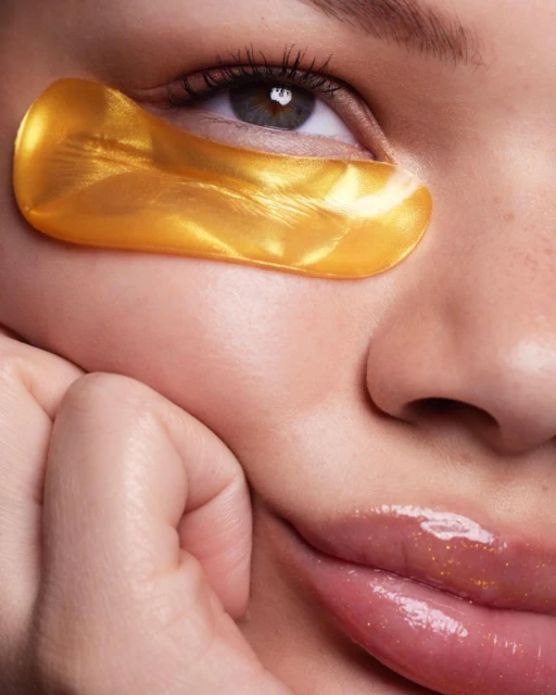 Close-up of a woman with a gold under-eye mask, showcasing beauty and skincare with focus on her eye, smooth skin, and glossy lips.