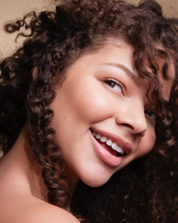 Close-up portrait of a smiling woman with voluminous dark curly hair and warm neutral makeup by photographer Candy Kennedy.