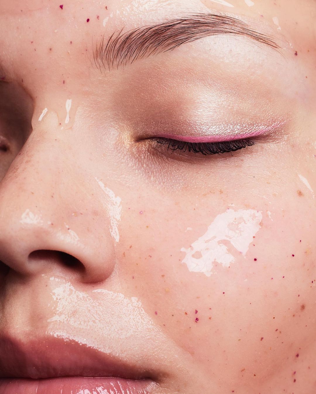 Close-up of a woman's face with glossy skin and pink eyeliner, showcasing beauty and skincare. Skin is dewy, giving it a fresh appearance.