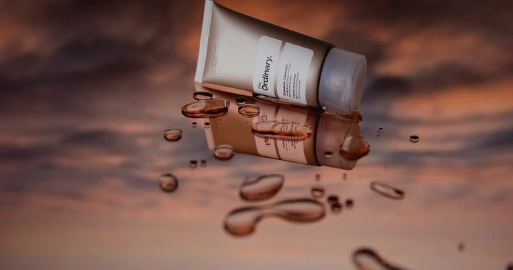 Beauty product photography featuring a tube of The Ordinary Squalane Cleanser reflecting on a wet surface with a dreamy sky background.
