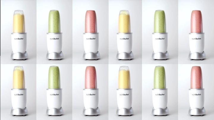 Multiple NutriBullet blenders filled with yellow, green, and red smoothies, arranged in a grid pattern against a white background.