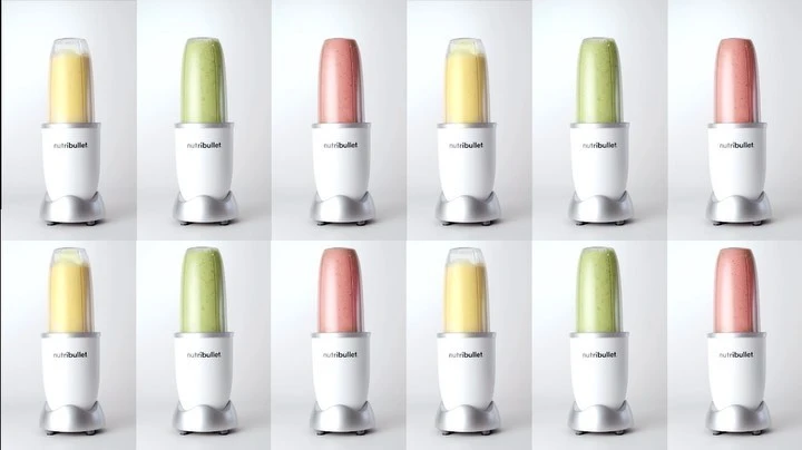 Multiple NutriBullet blenders filled with yellow, green, and red smoothies, arranged in a grid pattern against a white background.