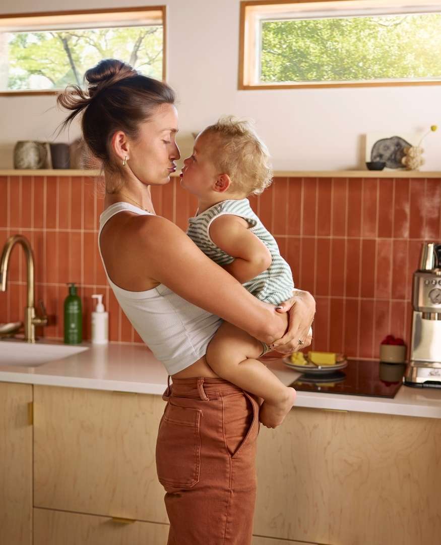 A mother holding her baby in a kitchen. The mother and child are close to each other in a modern home interior.