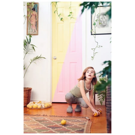 Child crouching on a patterned rug in a bright room with yellow and pink split-painted door, reaching for lemons.