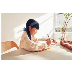 Young child writing in a notebook at a table in a sunlit room photographed by Candy Kennedy.