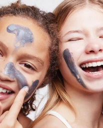 Close-up portrait of two young girls smiling with grey clay face masks applied on their skin