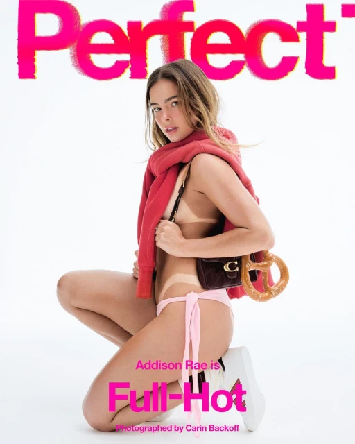 Addison Rae poses in a pink bikini and red sweatshirt holding a Coach purse with pretzel in a bright studio setting.
